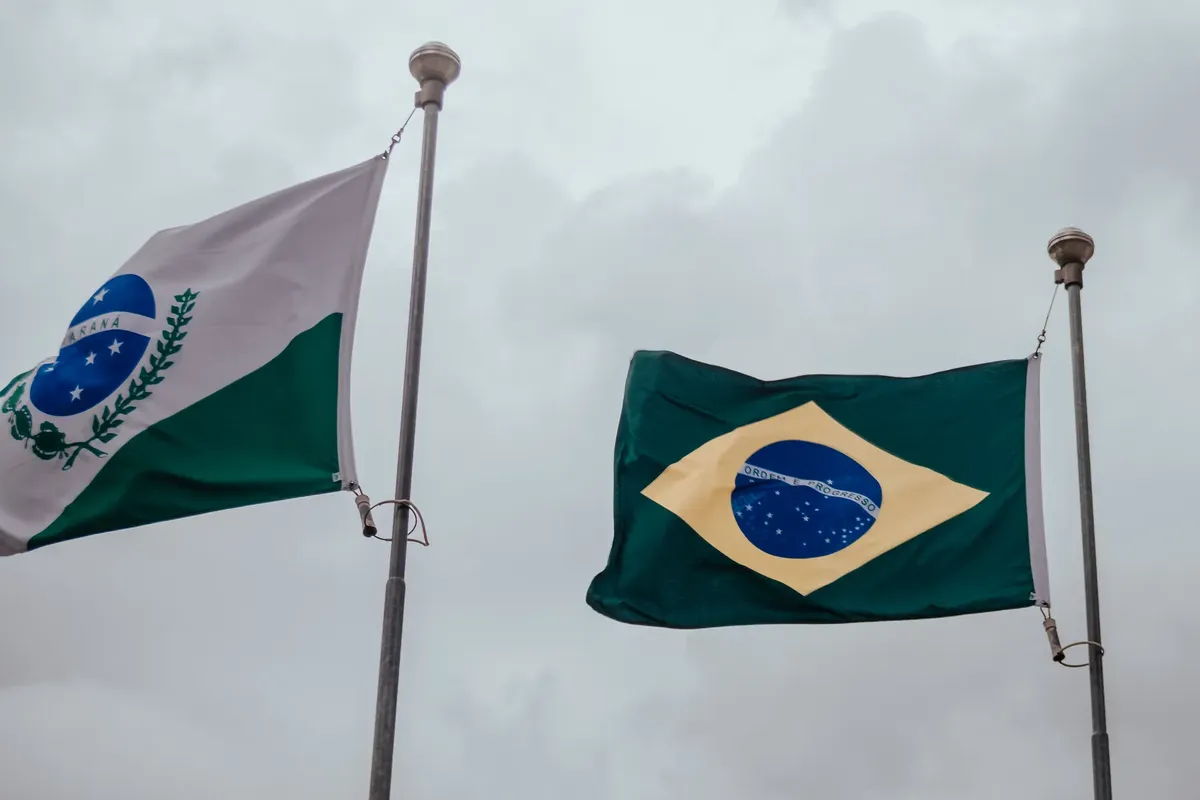 Brazil and Paraná flags against a cloudy sky, captured outdoors.