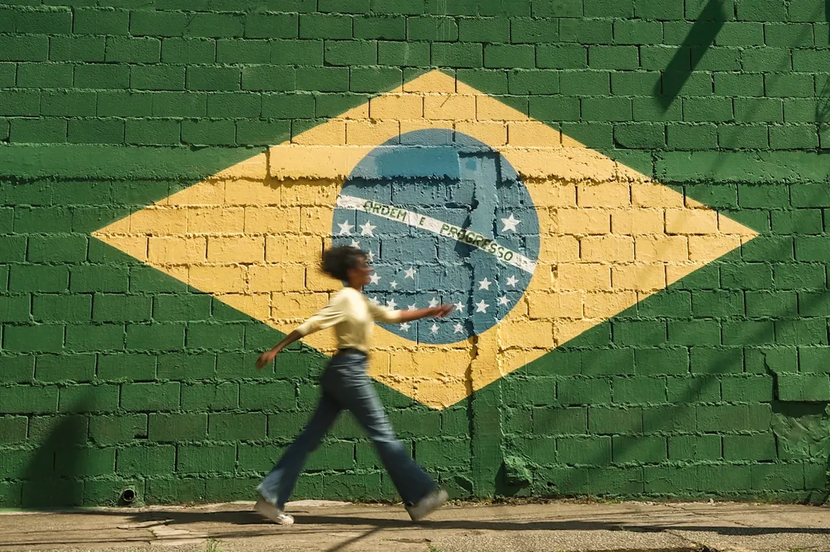 アフロアメリカンの女の子が、晴れた外道場にあるブラジル国旗の壁画の前を歩いている。