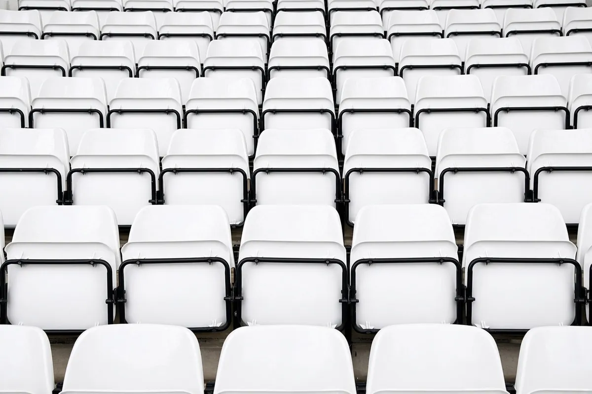 Leere weiße Stadionsitze mit schwarzen Armlehnen stehen in engen Reihen, und niemand sitzt darauf.